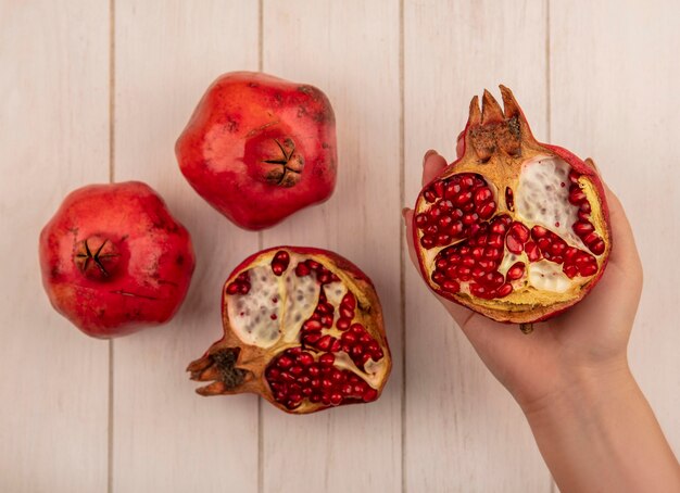 Kostenloses Foto draufsichtfrau, die halben granatapfel mit ganzem auf weißer wand hält