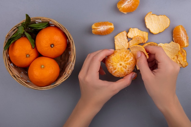 Draufsichtfrau schält Orange von der Schale mit Korb auf grauem Hintergrund