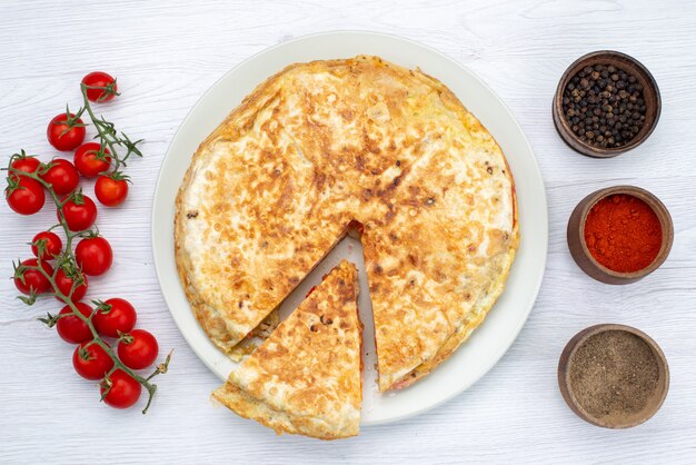 Draufsichtgebäck mit Gemüse nach innen mit frischen roten Tomaten und Gewürzen auf dem weißen Hintergrundgebäcknahrungsmittelmahlzeitgemüse