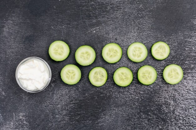 Draufsichtgurke geschnitten mit weißem Joghurt auf schwarzem Stein horizontal