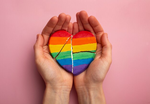 Draufsichthände, die gebrochenes Herz des Regenbogens halten