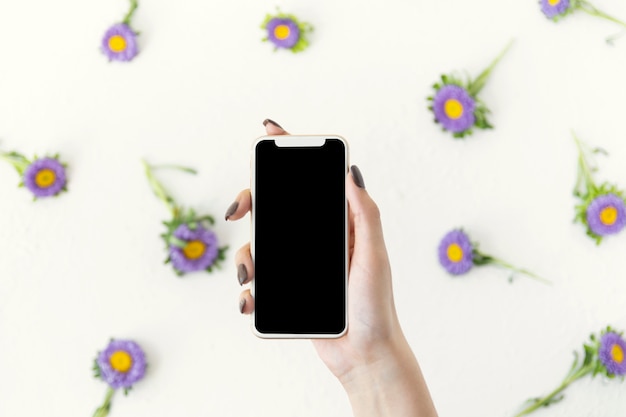 Draufsichthand, die ein Telefon umgeben durch Blumen hält