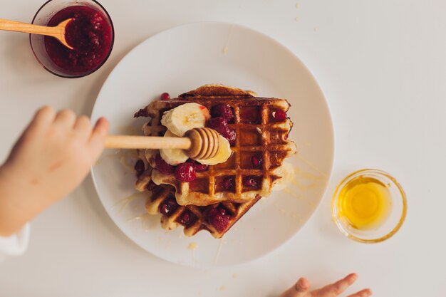 Draufsichthand, die Honig auf Waffel setzt