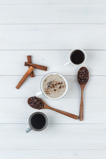 Draufsichtkaffee in den Tassen mit Kaffeebohnen, Zimtstangen auf hölzernem Hintergrund. vertikal