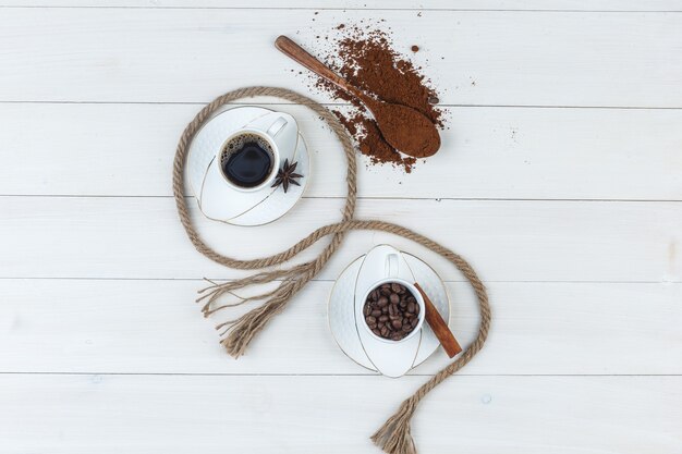 Draufsichtkaffee in der Tasse mit gemahlenem Kaffee, Gewürzen, Kaffeebohnen, Seil auf hölzernem Hintergrund. horizontal