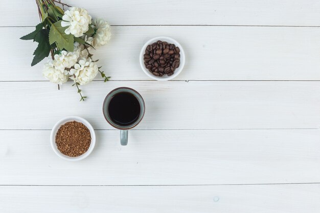 Draufsichtkaffee in der Tasse mit Kaffeebohnen, Blumen, gemahlener Kaffee auf hölzernem Hintergrund. horizontal