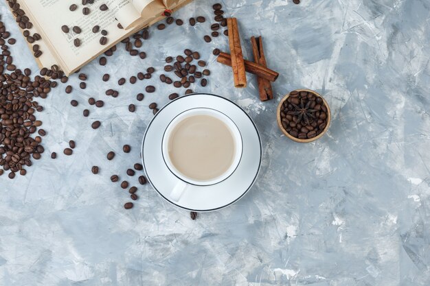 Draufsichtkaffee in der Tasse mit Kaffeebohnen, Buch, Zimtstangen auf grauem Gipshintergrund. horizontal