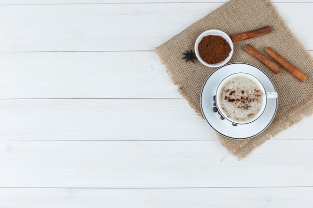 Draufsichtkaffee in der Tasse mit Kaffeebohnen, gemahlenem Kaffee, Gewürzen auf Holz und Stück Sackhintergrund. horizontal