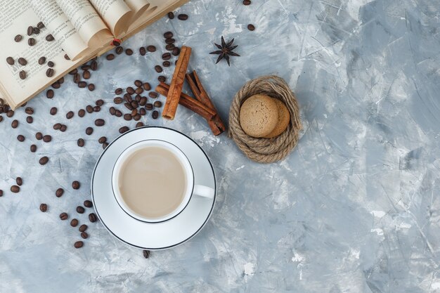 Draufsichtkaffee in der Tasse mit Keksen, Kaffeebohnen, Buch, Gewürzen auf grauem Gipshintergrund. horizontal