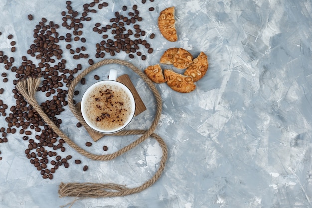 Draufsichtkaffee in der Tasse mit Keksen, Kaffeebohnen, Seil auf grauem Gips und Holzstückhintergrund. horizontal