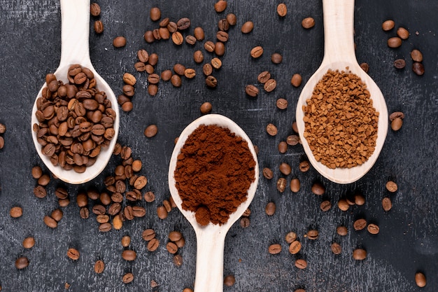 Draufsichtkaffeebohnen und Instantkaffee in den Holzlöffeln auf dunkler Oberfläche