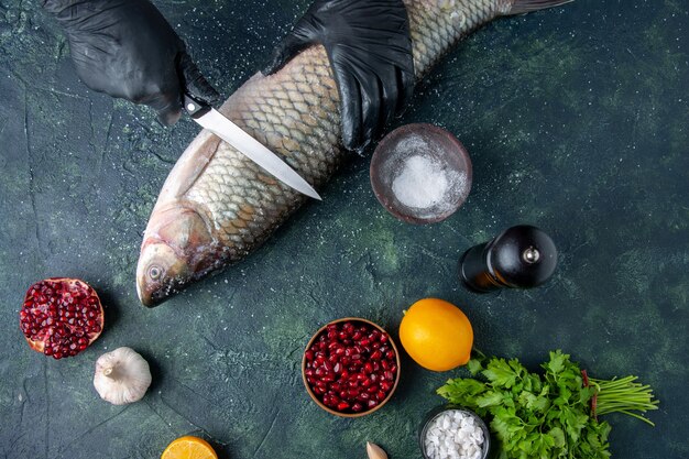 Draufsichtkoch mit Handschuhen, die rohen Fisch Pfeffermühle Granatapfelkerne in Schüssel auf dem Tisch schneiden