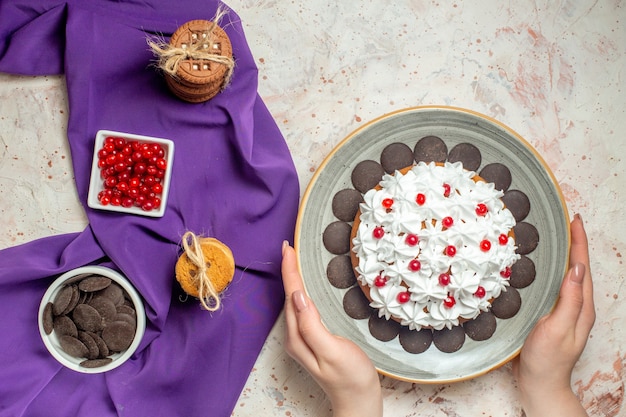Draufsichtkuchen auf Teller in Frauenhandplätzchen, die mit Seilschüsseln mit Beeren und Schokolade auf violettem Schal gebunden sind