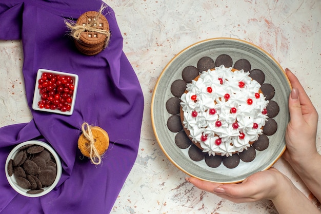 Draufsichtkuchen auf teller in weiblichen handplätzchen, die mit seilschüsseln mit beeren und schokolade auf violettem schal gebunden sind
