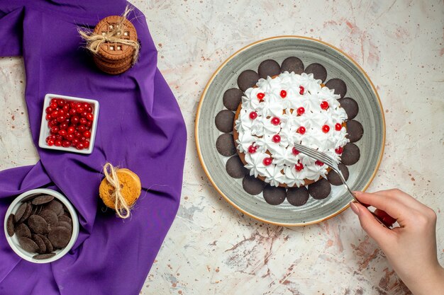 Draufsichtkuchen auf Tellerplätzchen, die mit Seilschüsseln mit Beeren und Schokolade auf lila Schalgabel in Frauenhand gebunden sind
