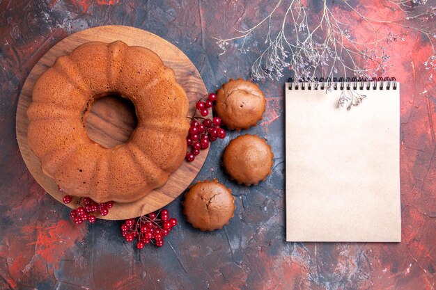 Draufsichtkuchen ein Kuchen mit roten Johannisbeeren die appetitlichen Cupcakes neben dem weißen Notizbuch