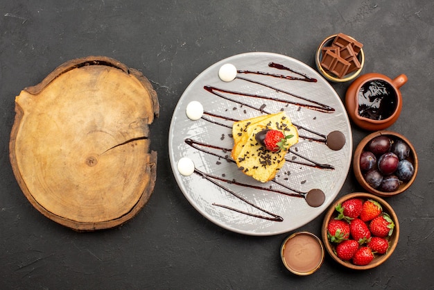 Draufsichtkuchen mit Erdbeer-Erdbeer-Schokolade und Beeren in Schalen und Kuchenteller mit Erdbeeren und Schokoladensauce neben dem Schneidebrett auf dem Tisch
