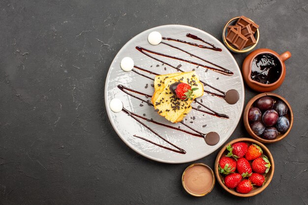 Draufsichtkuchen mit Erdbeer-Erdbeer-Schokolade und Beeren in Schalen und Teller mit Kuchen mit Erdbeeren und Schokoladensauce auf dem Tisch