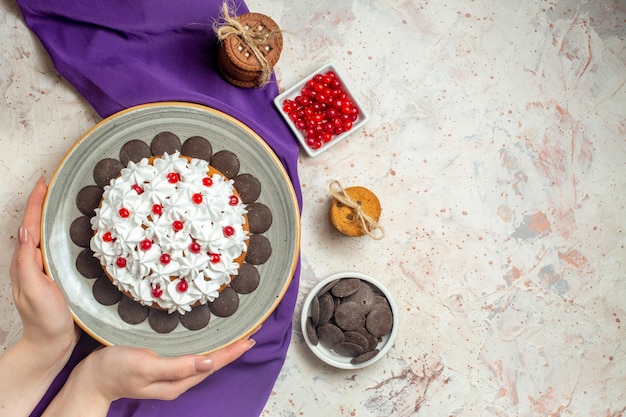 Draufsichtkuchen mit Gebäckcreme auf Teller in weiblicher Hand lila Schalkekse mit Seilbeeren in Schüssel gebunden