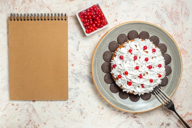 Draufsichtkuchen mit Gebäckcreme und Schokoladenbeere im Schüsselgabelnotizbuch