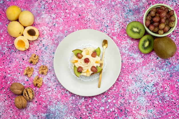 Draufsichtkuchen mit Sahne- und Fruchtscheiben zusammen mit Aprikosen und Kiwis auf der farbigen Hintergrundkuchenkeks-süßen Zuckerfarbe