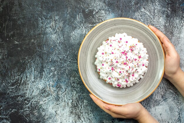 Draufsichtkuchen mit weißer gebäckcreme auf grauer runder platte in weiblicher hand auf grauem tisch mit freiem platz