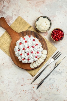 Draufsichtkuchen mit weißer gebäckcreme auf holzbrett auf zeitungsgabel und tafelmesserbeeren und weißer schokolade in schalen