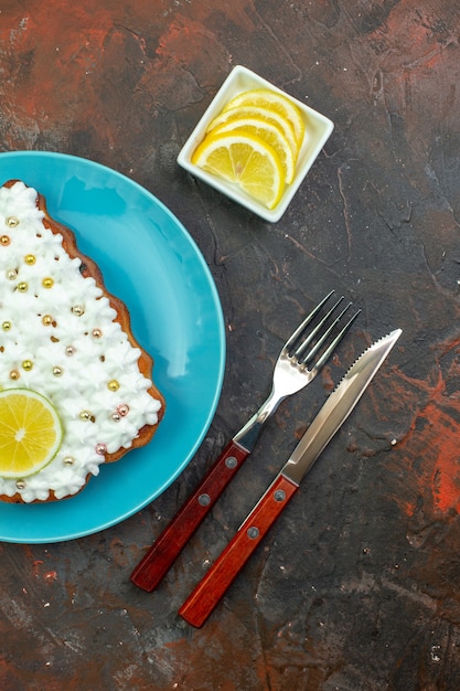 Draufsichtkuchen mit Zitrone auf blauem Teller Zitronenscheiben in Schüsselmesser und Gabel auf dunkelrotem Hintergrund