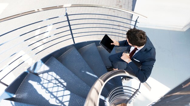 Draufsichtmann mit der Tablette, die auf Treppe steht