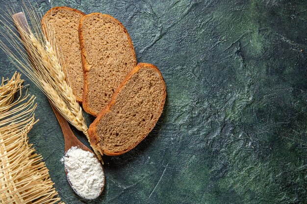 Draufsichtmehl auf Holzlöffel mit dunklen Brotlaibs auf dunklem Schreibtisch