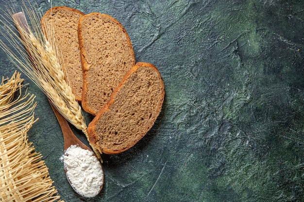 Draufsichtmehl auf Holzlöffel mit dunklen Brotlaibs auf dunklem Schreibtisch