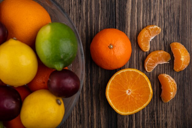 Draufsichtmischung der Früchte Zitronen Limetten Pflaumen Pfirsiche und Orangen in einer Vase auf einem hölzernen Hintergrund