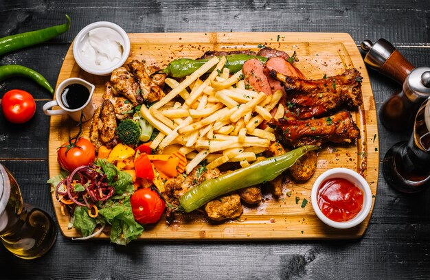 Draufsichtmischung von Fleischsnacks mit Pommes Frites gegrilltem Gemüsesalat und Saucen auf dem Brett