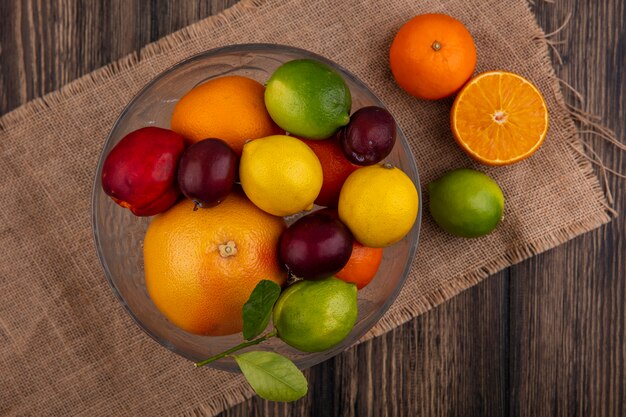 Draufsichtmischung von Früchten Zitronen Limetten Pflaumen Pfirsiche und Orangen in einer Vase auf einer beigen Serviette