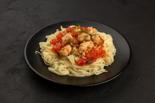 Draufsichtnudeln mit Hühnerflügeln und Tomatensauce in schwarzer Platte auf dem dunklen Boden gekocht