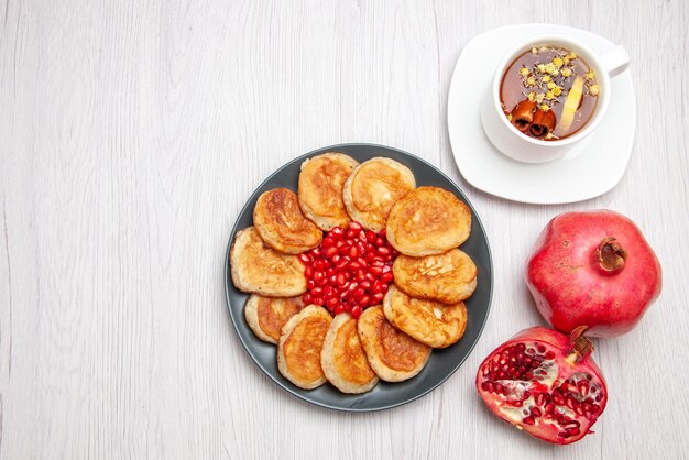 Draufsichtpfannkuchen und Granatapfel Teller mit appetitlichen Pfannkuchen Granatapfel und eine Tasse Kräutertee auf dem Tisch