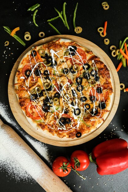 Draufsichtpizza auf einem Stand mit Tomatenoliven und Paprika auf schwarzem Tisch