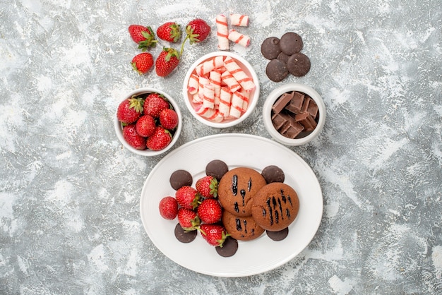 Draufsichtplätzchen-Erdbeeren und runde Pralinen auf den weißen ovalen Tellerschalen mit Bonbon-Erdbeer-Pralinen in der Mitte des grauweißen Tisches