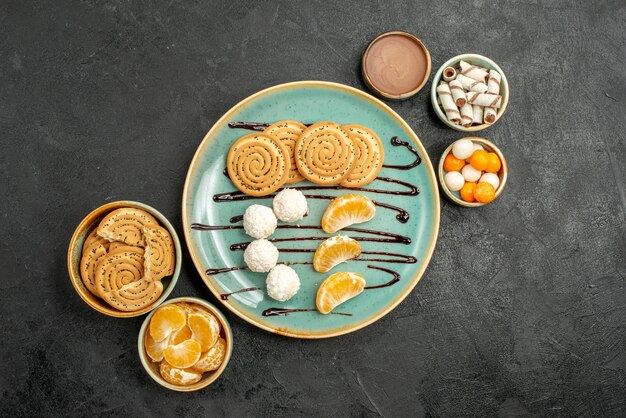 Draufsichtplätzchen und Bonbons mit Mandarinen auf grauem Tisch süßer Keksplätzchen