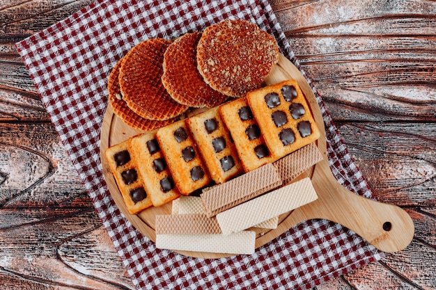 Draufsichtplätzchen und Waffeln auf Schneidebrett auf Stoff und hölzernem Hintergrund. horizontal