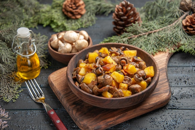 Draufsichtplatte an Bord Teller mit Kartoffeln und Pilzen auf Schneidebrett neben der Gabel unter Schüssel mit Pilzöl in Flasche und Zweigen mit Zapfen