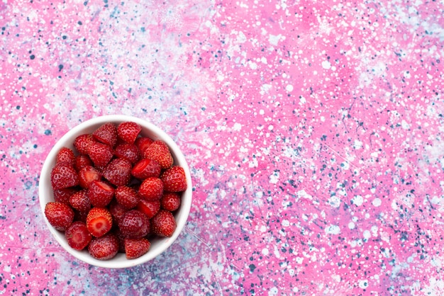 Draufsichtplatte mit Erdbeeren roten frischen milden Erdbeeren auf der farbigen Schreibtischfruchtbeerenfarbe reif