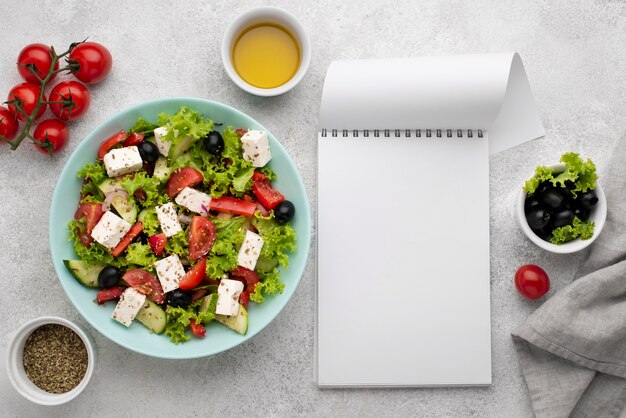 Draufsichtsalat mit Feta-Käse, Tomaten und Oliven mit leerem Notizblock