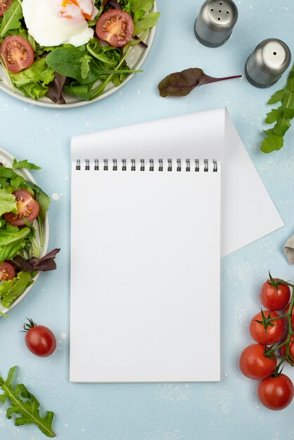 Draufsichtsalat mit Spiegelei und Tomaten mit leerem Notizbuch