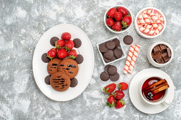 Draufsichtschalen mit Bonbons Erdbeerpralinen Bonbons und einigen Erdbeersüßigkeiten Pralinen und einer Tasse Tee auf dem grauweißen Grund