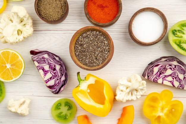 Draufsichtschalen mit Gewürzen schneiden gelben Paprika Blumenkohl geschnittenen Rotkohl schneiden grüne Tomaten auf Holztisch stock photo