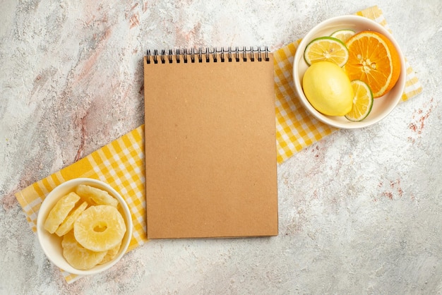 Draufsichtteller auf dem cremefarbenen Notizbuch der Tischdecke und Teller mit getrockneten Ananas und Zitrusfrüchten auf der karierten Tischdecke