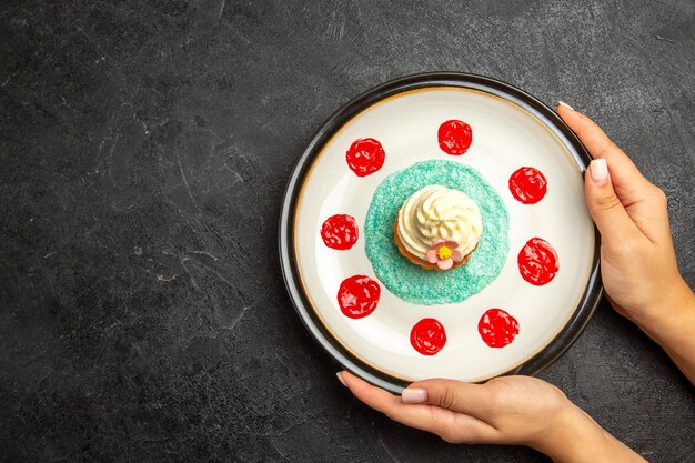 Draufsichtteller mit Cupcake appetitlicher Cupcake auf dem weißen Teller in den Händen auf dem dunklen Hintergrund