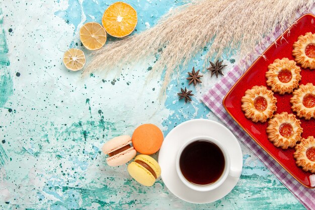 Draufsichtzuckerplätzchen innerhalb der roten Platte mit Tasse Tee und Macarons auf dem blauen Hintergrund