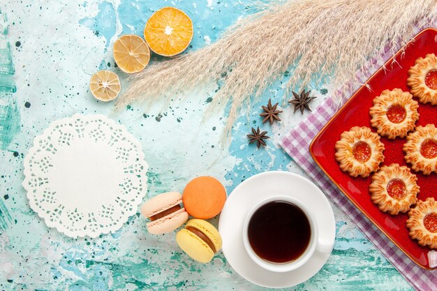 Draufsichtzuckerplätzchen innerhalb der roten Platte mit Tasse Tee und Macarons auf dem blauen Hintergrund